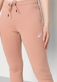 Närbild av en person som bär rosa Nike träningsbyxor med dragsko i midjan och vit broderad logotyp på låret.