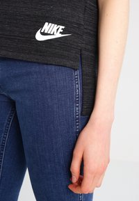 Black athletic top with a regular fit, featuring a white Nike logo, textured fabric, and a side slit. Paired with blue denim jeans.