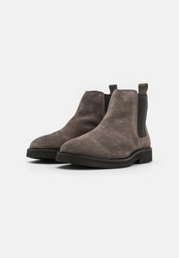 Botas Chelsea de ante gris con paneles laterales elásticos, puntera redondeada y suela de goma negra texturizada. Incluyen tiradores para facilitar su uso.