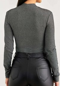 Maglione grigio a coste con maniche lunghe e colletto alto, abbinato a pantaloni in ecopelle nera con tasche e una texture liscia.