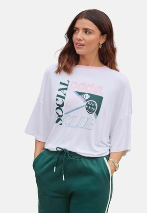 Hvid oversized t-shirt med grafiktryk med teksten "Social Padel Club", kombineret med mørkegrønne joggers med sidelængder.