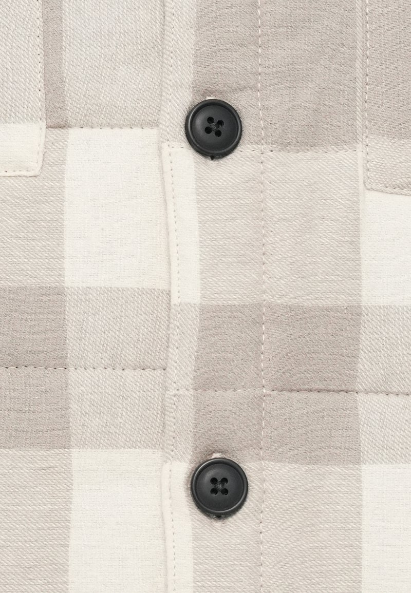 Hellbeige und weiße karierte Stoff mit vertikaler Naht und zwei schwarzen vierlochgarnituren.