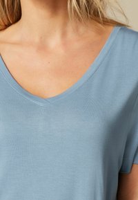 Lichtblauwe t-shirt met korte mouwen en v-hals, gemaakt van zacht materiaal, met een subtiele glans en nette stiksels langs de halslijn.
