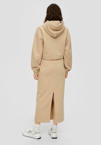 Beige hoodie gecombineerd met een bijpassende rok met een split aan de achterkant. Materiaal ziet er zacht en glad uit. Witte sneakers maken de look compleet.