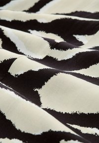 Baumwollstoff mit einem schwarz-weißen abstrakten Muster und auffälligen Pinselstrich-Streifen. Die Textur wirkt glatt und leicht matt.