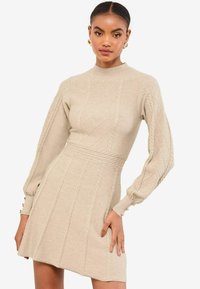 Beige stickad klänning med hög krage, långa puffärmar och diamantsmönster. Den har en åtsittande midja och en utsvängd kjol.