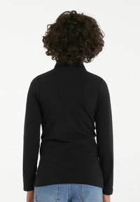 Schwarzes Langarm-Turtleneck-Shirt aus glattem Stoff, figurbetontes Design, kombiniert mit hellblauen Jeans, Ansicht von hinten.