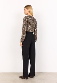 Långärmad leopardsmönstrad topp med rund halsringning, matchad med högmidjade svarta vida byxor och bruna slip-in skor med nitar.