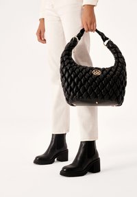 Czarna pleciona skórzana torebka z skręconym uchwytem i złotym akcentem logo. Posiada strukturalny kształt i gładką fakturę.