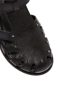 Sandal in pelle nera con ritagli, dettagli borchiati e suola intrecciata. Il design open-toe offre traspirabilità e stile.