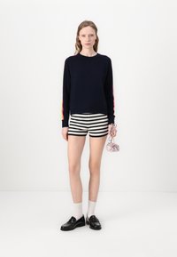 Navy sweater with multicolor stripes on sleeves, black and white striped shorts, black loafers, and a small pink bag.