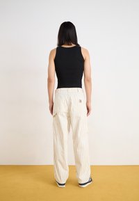 Schwarzes, geripptes Tanktop, kombiniert mit lockeren, hellen gestreiften Hosen. Verfügt über große Taschen und lässiges Schuhwerk. Einfaches, funktionelles Design.
