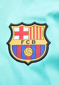 Λογότυπο της FC Barcelona με κόκκινος σταυρό, κόκκινες και κίτρινες ρίγες και μπλε και κόκκινες κάθετες ρίγες σε φόντο από τιρκουάζ ύφασμα.
