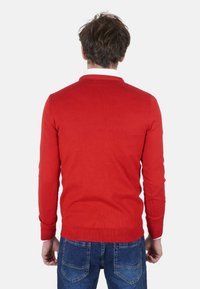 Maglione rosso a maglia con maniche lunghe e scollo arrotondato, realizzato in materiale morbido. Abbinato a jeans di denim blu, vista posteriore.