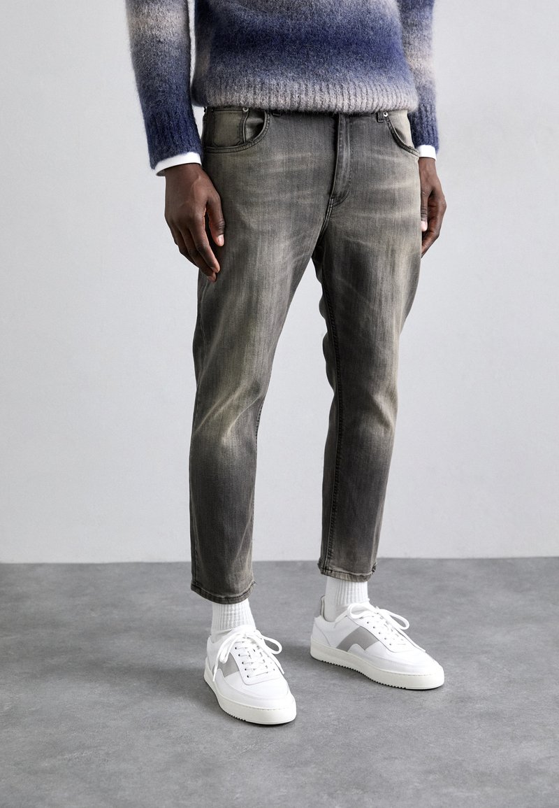 Grå denimjeans med en falmet finish, fem lommer og innsnevret ben, sammen med hvite sneakers og en stripete grå og blå genser.