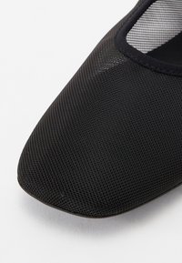 Chaussure en tissu mesh noir avec bout carré arrondi et bord élastiqué le long de l'ouverture sur fond blanc.