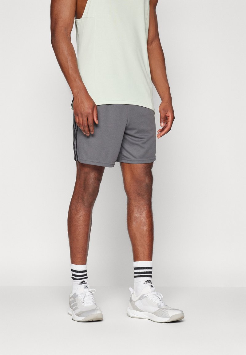Gray athletic shorts with side stripes, paired with white sneakers and striped socks. The tank top is a light green color, sleeveless.