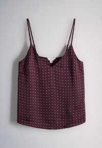 Sleeveless purple camisole top with thin adjustable straps and a small white polka dot pattern hanging against a light wall.