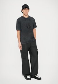 Svart kortermet denimskjorte, cargobukser med flere lommer, svart caps og svarte sko med hvite detaljer. Enkel, moderne design.