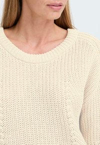 Kremfarget strikket genser med ribbet rund hals og teksturert strikkemønster som fremhever et lett og uformelt design.