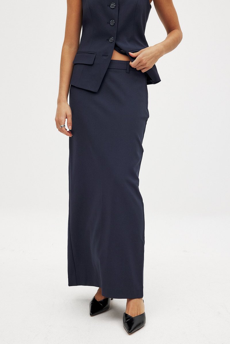 Marineblaue maßgeschneiderte Rock mit gerader Silhouette, leichtem Stoff, seitlichem Schlitz und kombiniert mit einem passenden ärmellosen Blazer.