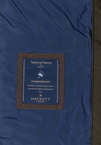 Tkanina u mornarsko plavoj boji otporna na vodu s smeđom etiketom na kojoj piše "Tehničke tkanine od Hacketta." Tekst uključuje upute za njegu i brendiranje.