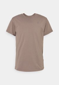 T-shirt à col rond à manches courtes, taupe uni, avec des poignets de manches subtilement retroussés et un petit logo sur la poitrine, sur fond blanc.