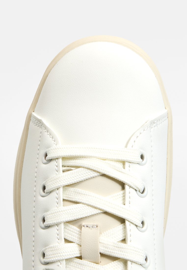 Baskets blanches avec un cuir lisse, une forme arrondie, des lacets plats et une semelle en caoutchouc beige clair avec des coutures minimales.