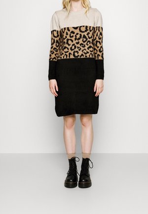 Vrouw draagt een beige, luipaardprint en zwart kleurblok trui-jurk met lichtbruine sokken en zwarte veterlaarzen.