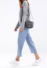 Šedý svetr s červenou výšivkou, krátké kalhoty modro-bílé pruhované, bílé perforované tenisky, doplněné černou kabelkou s hadím potiskem.