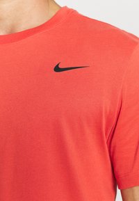 Zbliżenie na osobę w czerwonej koszulce Nike z czarnym logo swooshu umieszczonym na górnej części klatki piersiowej.