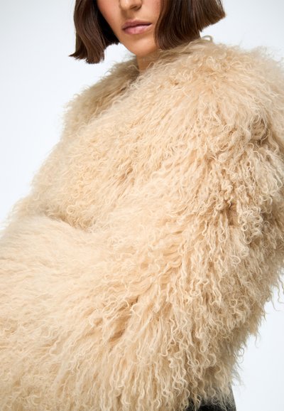 Beige fuzzy sweater made of textured yarn, featuring voluminous curly fibers and a loose fit, with wide sleeves and a cozy appearance.