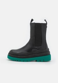 Stivale Chelsea nero realizzato in pelle liscia, dotato di pannelli laterali elastici, linguetta per una facile indossabilità e una audace suola in gomma verde.