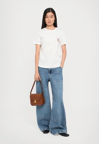 White cotton t-shirt with a bunny graphic on the chest, paired with wide-leg blue denim jeans and a brown bag. Textured and modern.