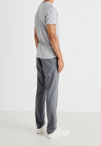 T-shirt grigio a maniche corte, in morbido cotone, abbinato a pantaloni grigi e sneakers bianche, in piedi su uno sfondo neutro.