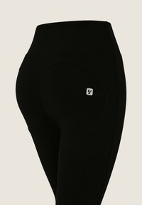 Leggings neri a vita alta con una texture liscia, caratterizzati da cuciture curve e un piccolo logo sulla tasca posteriore.