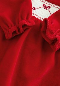 Tessuto rosso con bordi arricciati e un motivo testurizzato. Presenta ricami bianchi con dettagli rossi al centro. Texture morbida e liscia.