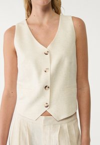 Linnen mouwloos vest in lichtbeige met een V-hals, vijf knopen en zijzakken, uitgevoerd in een licht gestructureerde stof.