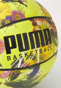 Puma košarkaška lopta sa žutom bazom, koja sadrži cvjetni uzorak. Teksturirana površina sa crnim brendingom; izraženi grip i šavovi.