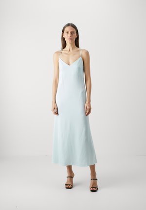 Un vestito midi senza maniche di colore azzurro chiaro con scollatura a V, presenta una texture liscia e una silhouette fluida, abbinato a sandali neri con cinturini.