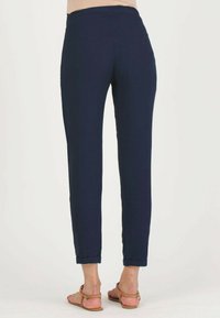 Navy blue trousers made of textured fabric, featuring a slim fit, rolled cuffs, and a mid-rise waist. Worn with tan flat sandals.