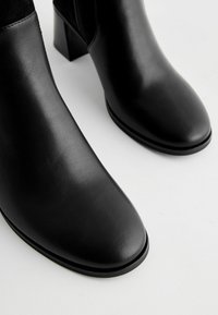 Bottines noires en cuir lisse, avec un bout carré et un talon bloc modéré. Design minimaliste sans matériel visible.
