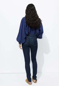 Blouse marine avec des manches volumineuses, associée à un jean foncé ajusté. Le jean présente des poches arrière et un design taille haute.