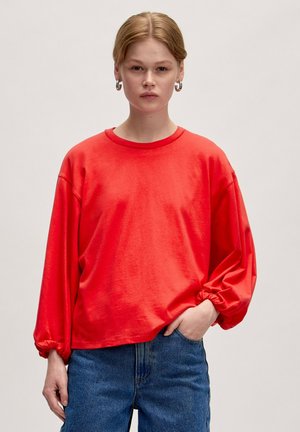 Roter Langarm-Sweatshirt mit herunterhängenden Schultern, lockerer Passform, geripptem Rundhalsausschnitt und elastischen Bündchen, kombiniert mit blauen Jeans.
