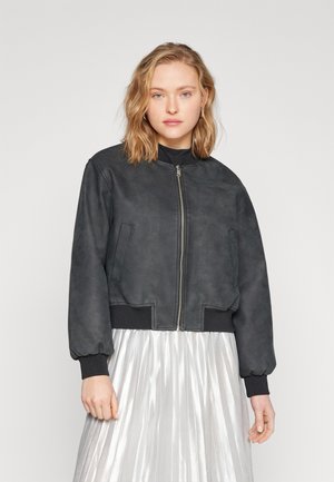 Černá semišová bomber bunda se zipovým uzávěrem, žebrovanými manžetami a pasem. Model nosí pod ní plisovanou stříbrnou sukni.
