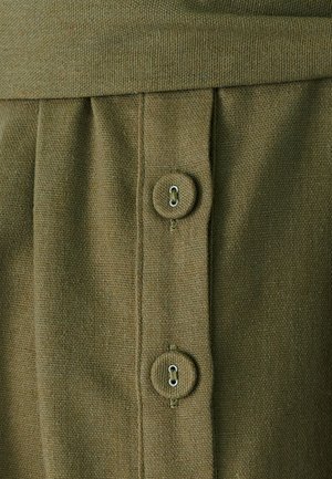 Olivově zelená látka s texturovaným povrchem, obsahující dva knoflíky a nařasené detaily podél švu. Jednoduchý a funkční design.