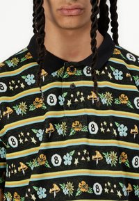 Svart polo skjorte med krage som har fargerike blomster- og geometriske mønstre, striper i gult, blått og grønt, og en knappestolpe.