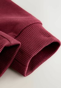 Burgundyröd sweatshirt ärm med ribbat mönster och slät tyg. Har en klassisk design med en vikning för en snug passform.
