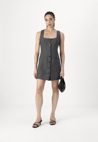 Šedé pruhované šaty s hranatým výstřihem, předními knoflíky a dvěma kapsami. V kombinaci s černými sandály na tenkých páskách a malou černou kabelkou.