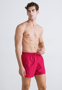 Boxeri de baie roșii cu talie elastică și șnur. Material ușor, lungime până deasupra genunchiului și textură netedă.